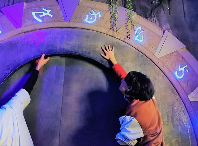 Trois joueurs manipulent un grand cadran circulaire illuminé en violet dans Atlantis : l'île secrète