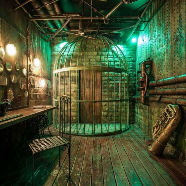 Décor steampunk aux teintes vertes, cage métallique, murs ornés de hublots lumineux chez Escape the Arrow