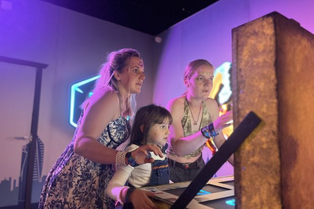 Deux femmes et une fillette devant un panneau lumineux dans une salle éclairée de violet, Cube Challenges, Team Square
