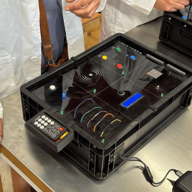 Boîtier noir à boutons, fils et clavier posé sur une table en inox, Stop The Bomb