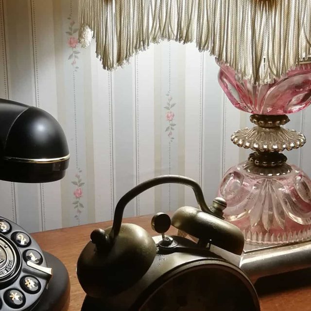 Téléphone vintage noir, lampe rétro et flacon de parfum rose dans la salle L'Hôtel des oubliés