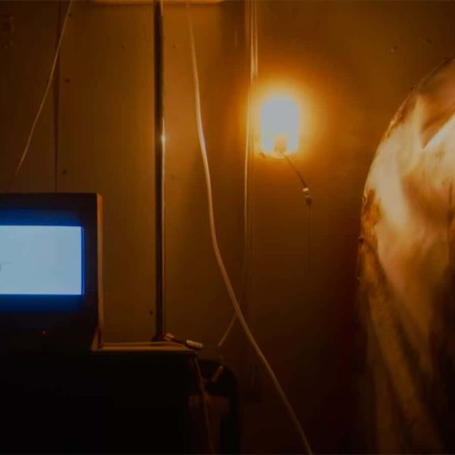 Petit écran allumé, lampe et personnage en blouse blanche dans une pièce faiblement éclairée, salle La secte chez Freeing à Saint-Maximin