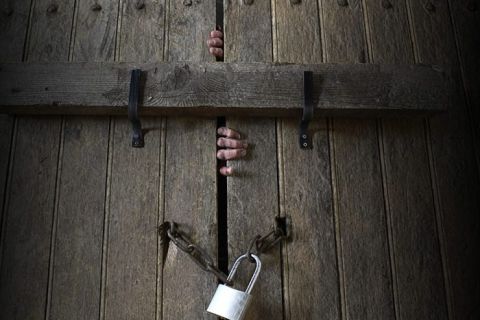 Porte en bois massif avec chaînes et cadenas, mains pressées contre le bois, ambiance carcérale de L'Asile