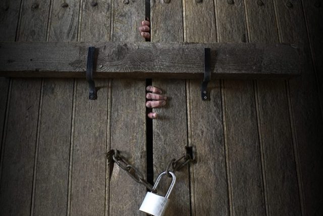 Porte en bois massif avec chaînes et cadenas, mains pressées contre le bois, ambiance carcérale de L'Asile