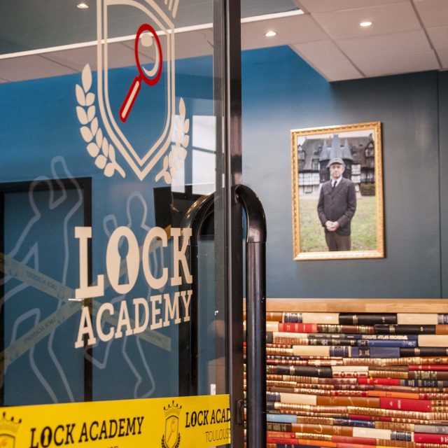 Entrée vitrée Lock Academy avec portrait encadré et mur de livres colorés, enseigne Lock Academy à Toulouse