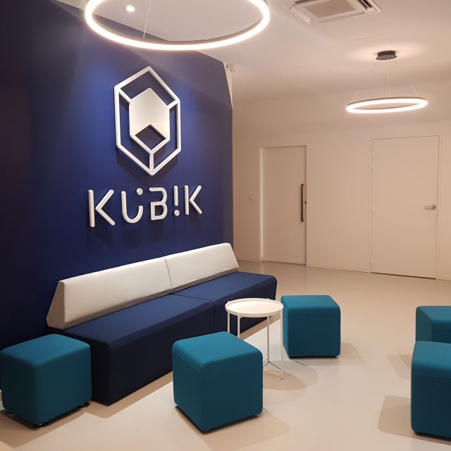 Espace d'accueil bleu nuit avec banquette blanche, pouf turquoise et logo Kubik au mur, Kubik à Paris