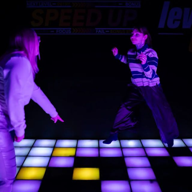 Deux joueurs face à face sur un damier lumineux violet, enseigne Speed Up Level Up, salle Level UP à Besançon