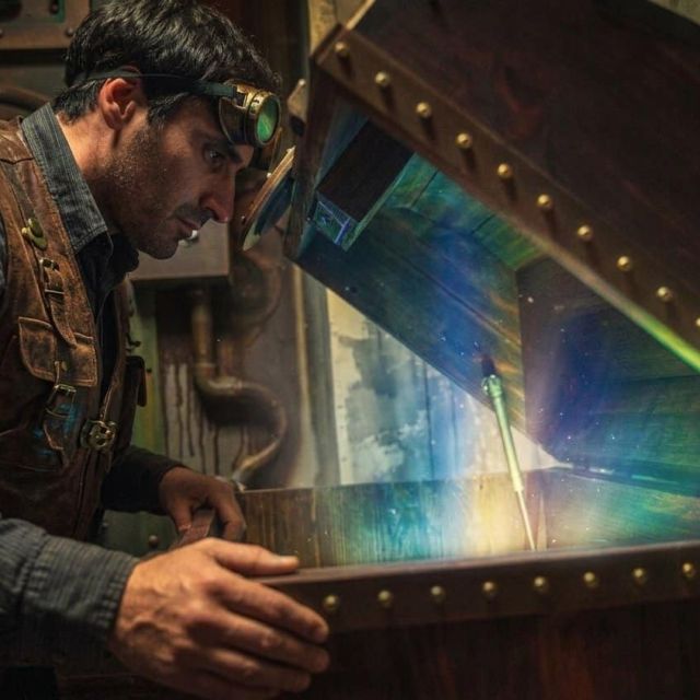 Homme penché sur un grand coffre ouvert d'où jaillit une lumière irisée, salle Steampunk chez BlackOut Room à Nice