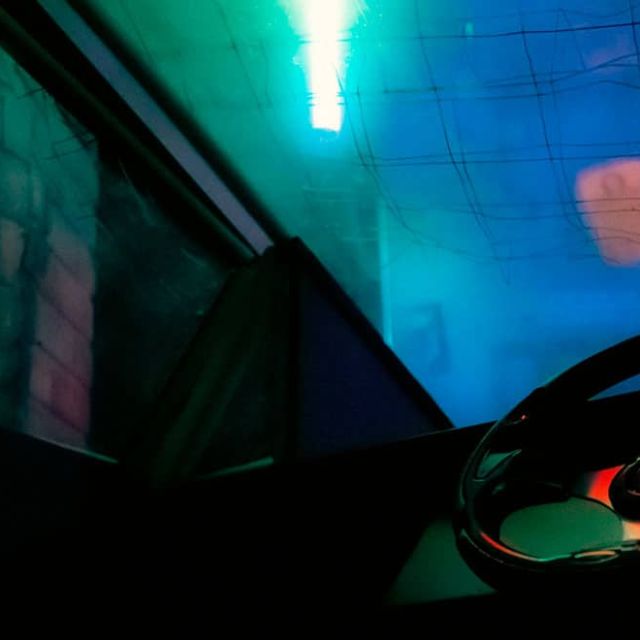 Volant de véhicule dans une cabine éclairée de vert et de rose, salle Alpha District chez Escape Time à Mulsanne
