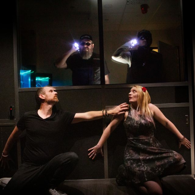Scène sombre de braquage où deux silhouettes éclairent la pièce à la lampe, salle Le Casse du Siècle chez The Box Escape Games