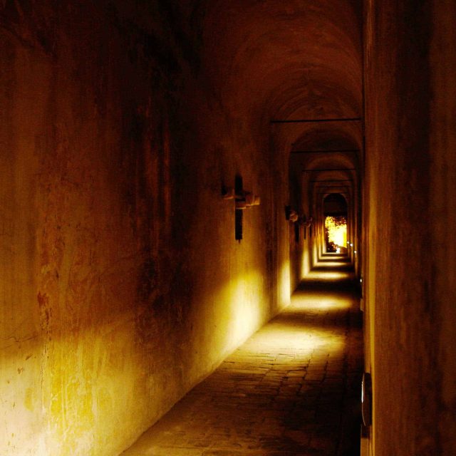Couloir souterrain aux murs en pierre ocre, éclairage jaune chaud créant des ombres allongées