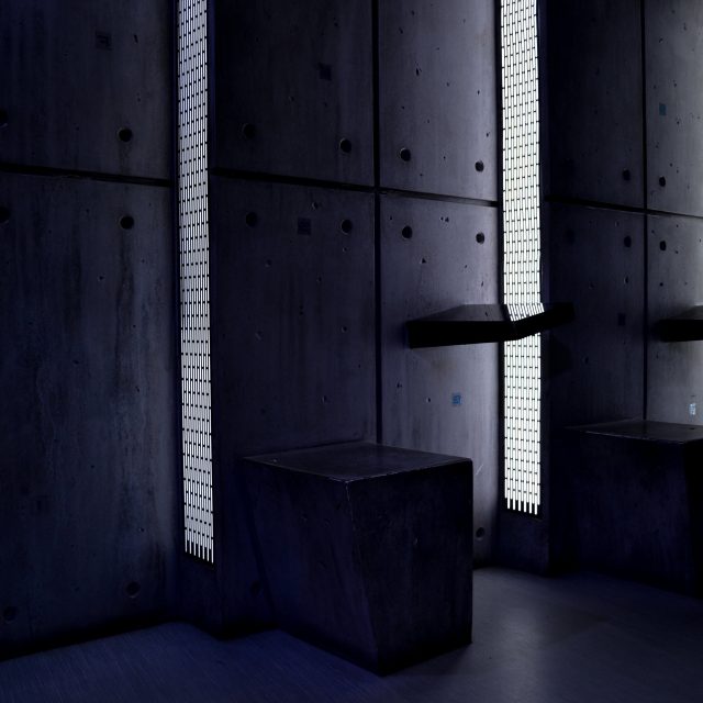 Cellule souterraine minimaliste aux murs béton, éclairage bleu froid et mobilier noir chez Prizoners à Paris