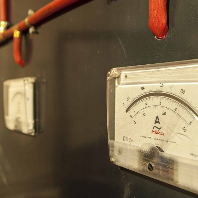 Ampèremètre vintage et disjoncteurs sur panneau électrique dans une salle de BREIZH ESCAPE