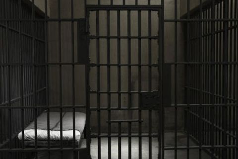 Cellule de prison aux barreaux noirs avec un lit au matelas blanc, salle Piégés chez Escape Yourself à La Rochelle