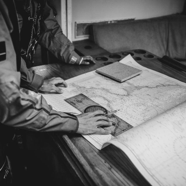 Mains sur une carte marine dépliée à bord d'un bateau, photo en noir et blanc, Les Aventures de Trifon à La Rochelle