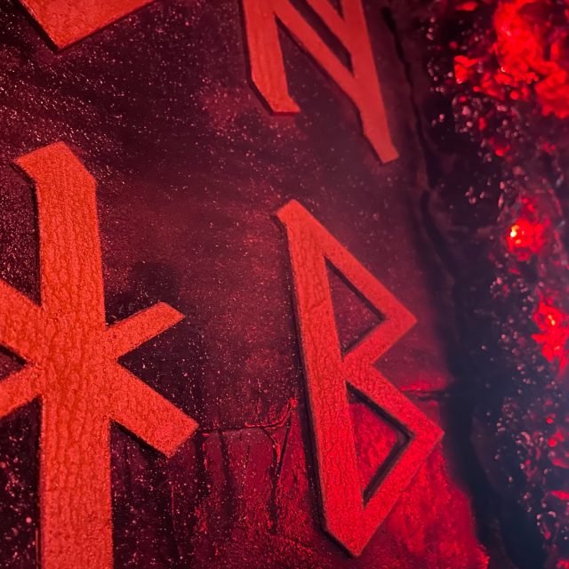 Symboles runiques rouges brillants sur une paroi noire, salle Les secrets de la Moria chez Escape The Movie à Marseille