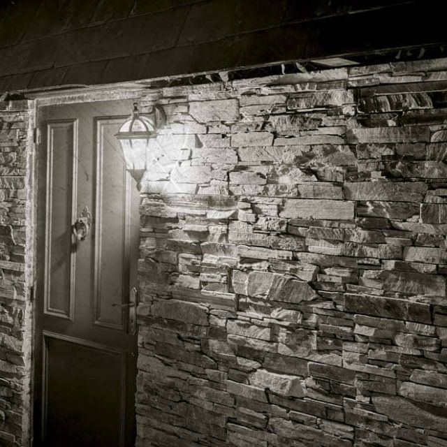 Mur de pierres avec volets et porte, image en noir et blanc, salle Le manoir des sœurs Aubépine chez Escape Time à Angers