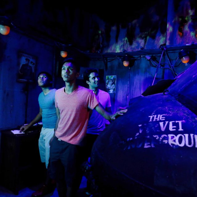 Trois joueurs dans un couloir souterrain aux néons bleus et violets chez Lockbusters Escape Game Orlando