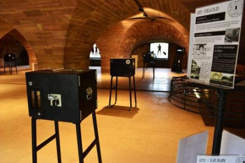 Grande salle voûtée de brique avec boîtes noires sur pieds et panneau explicatif, salle Perceurs de coffres à Belfort