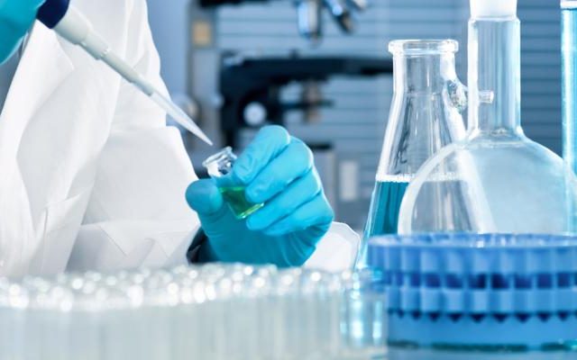 Main gantée de bleu versant un liquide dans une fiole de laboratoire, salle L'antidote secret chez Cinsens à Agde
