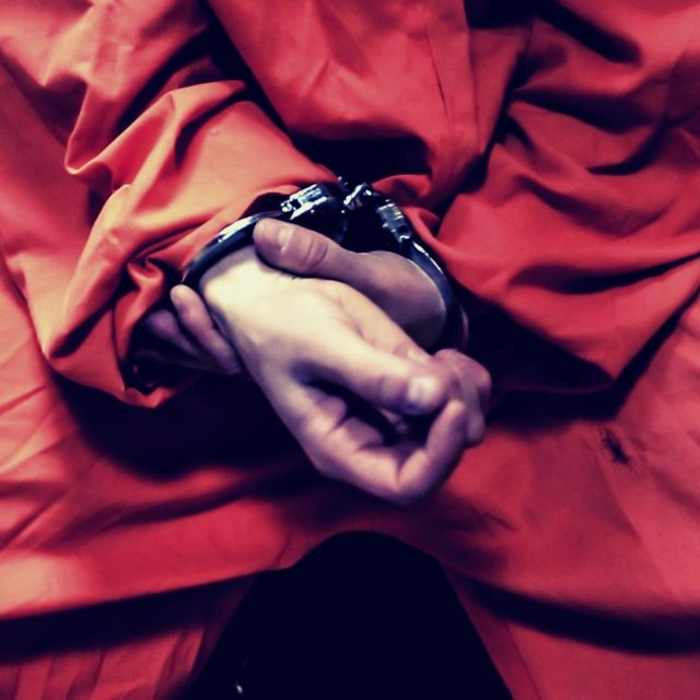 Mains tenant un mécanisme de détonation sur tissu rouge, dans La Prison Gal'Roa