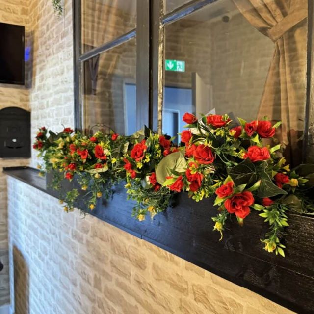 Jardinière de fleurs rouges devant une cloison vitrée et un mur de brique blanche, décor des salles d'Escape Factory à Guérande