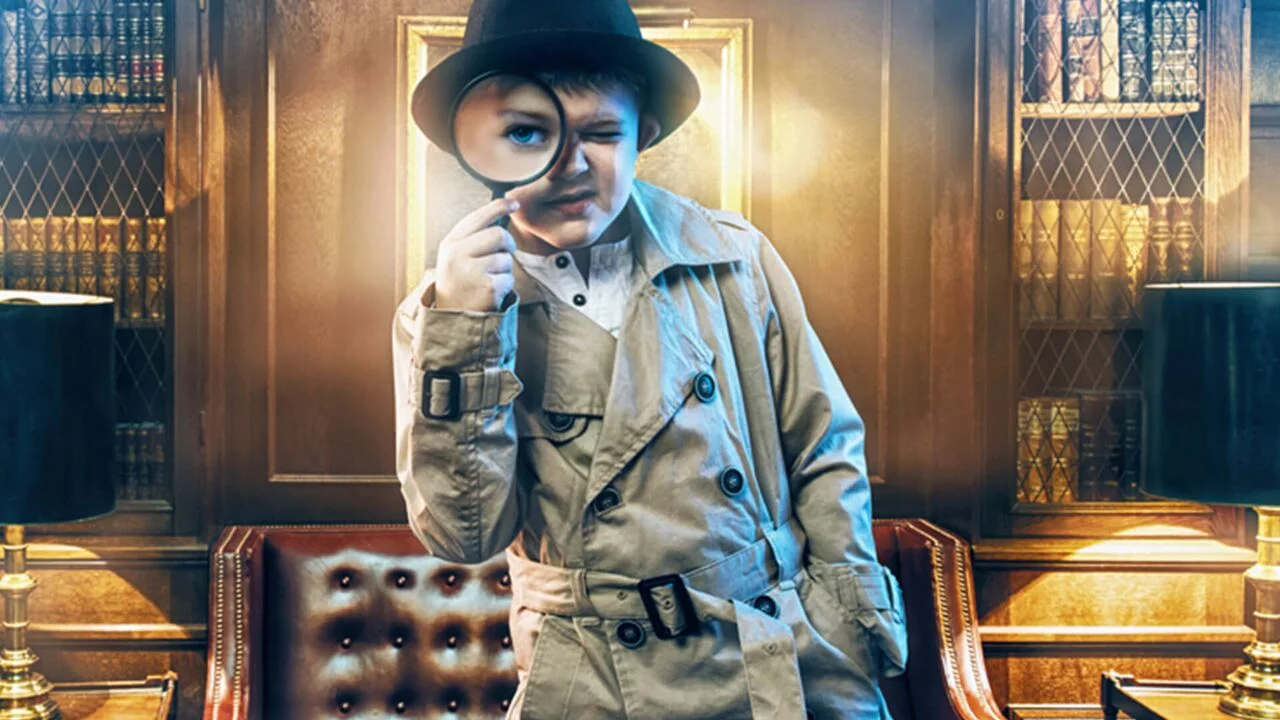 Enfant en trench et chapeau de détective regardant à travers une loupe, salle Le musée hanté chez Kid'Scape à Beynost